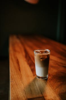 Refreshing glass of iced coffee with a gradient effect, placed on a rustic wooden table in ambient lighting.