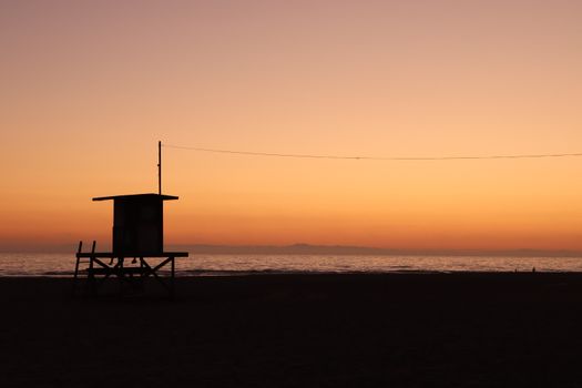 Lifeguard tower silhouette against a vivid Newport Beach sunset with a tranquil sea view.
