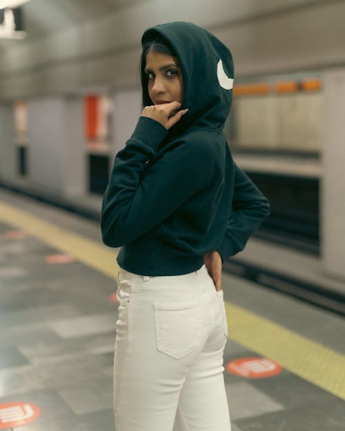 A woman in white pants and a black hoodie standing on a subway platform