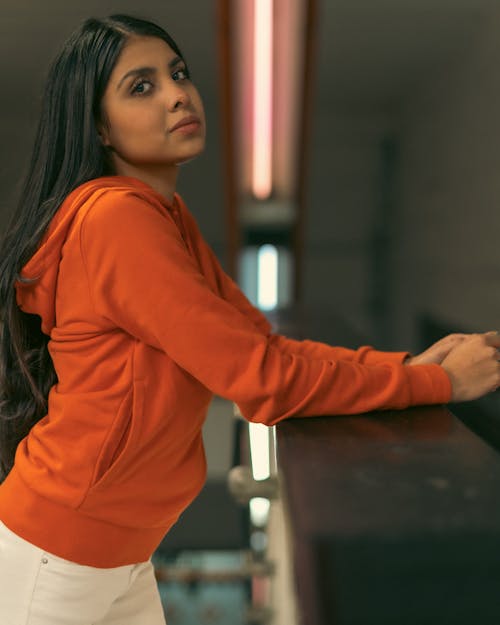 A woman in an orange hoodie leaning against a railing