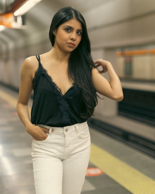 A woman in white pants and a black top standing in a subway station