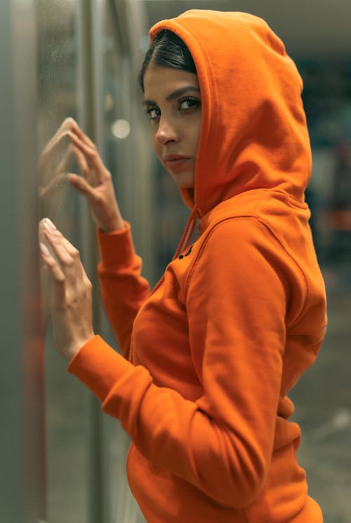 A woman in an orange hoodie leaning against a wall