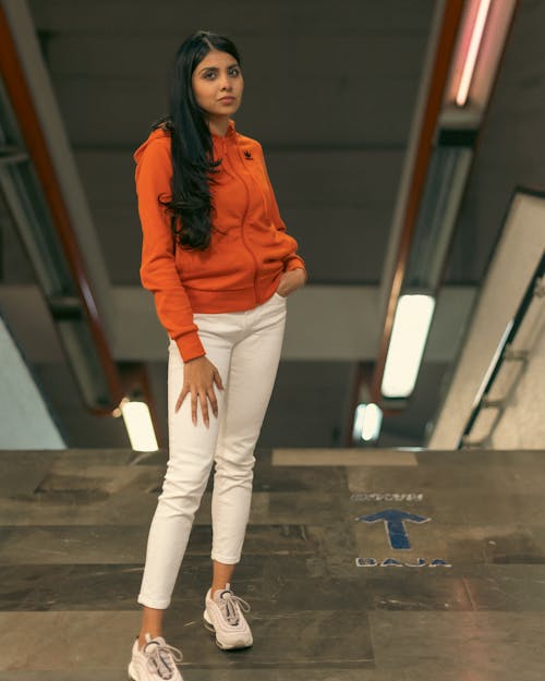 A woman in an orange sweatshirt and white pants