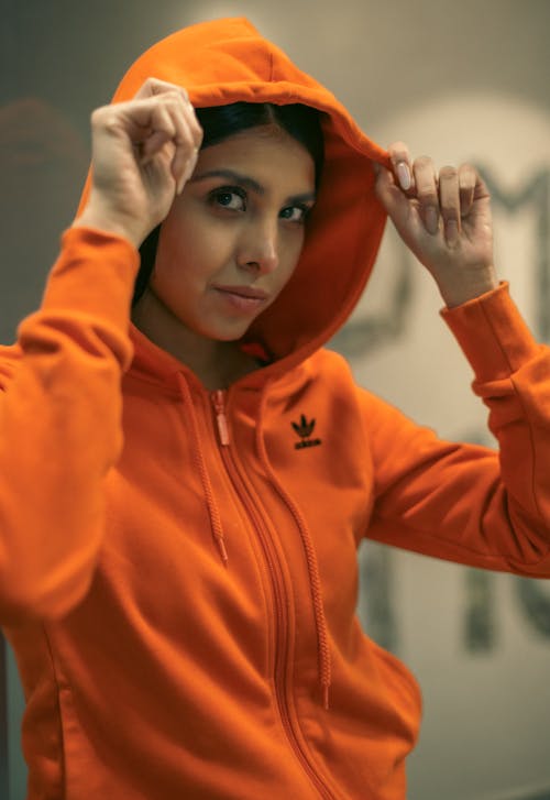 A woman in an orange hoodie is holding up her hand