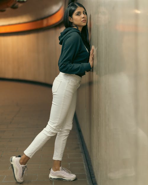 A woman leaning against a wall wearing white pants
