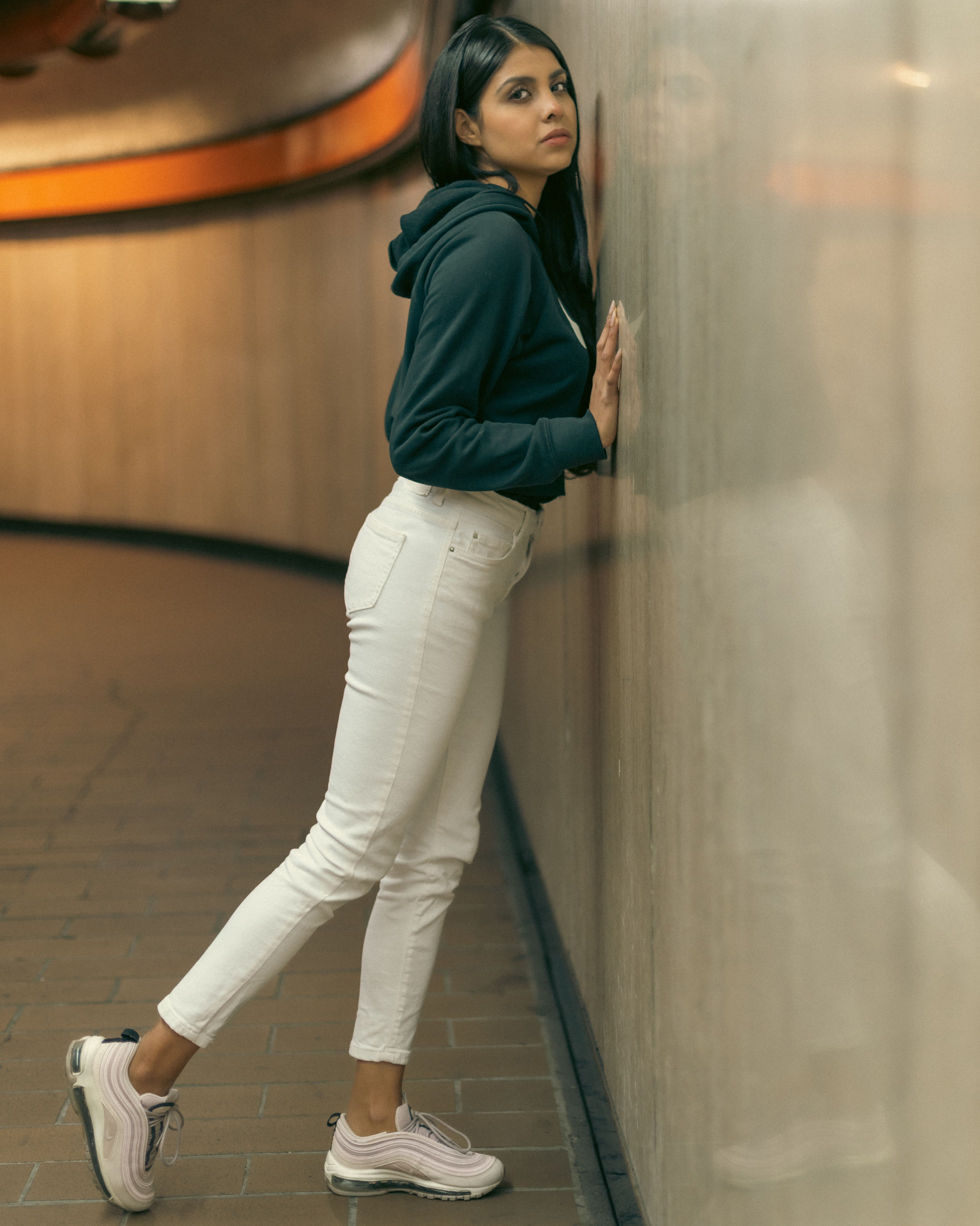 A woman leaning against a wall wearing white pants · Free Stock Photo