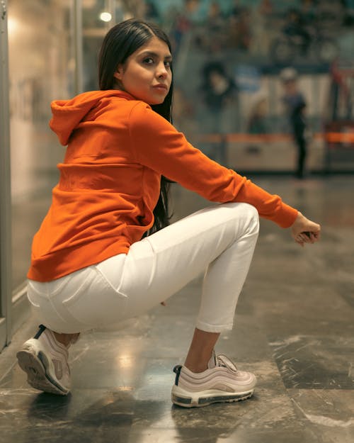 A woman squatting down in an orange hoodie