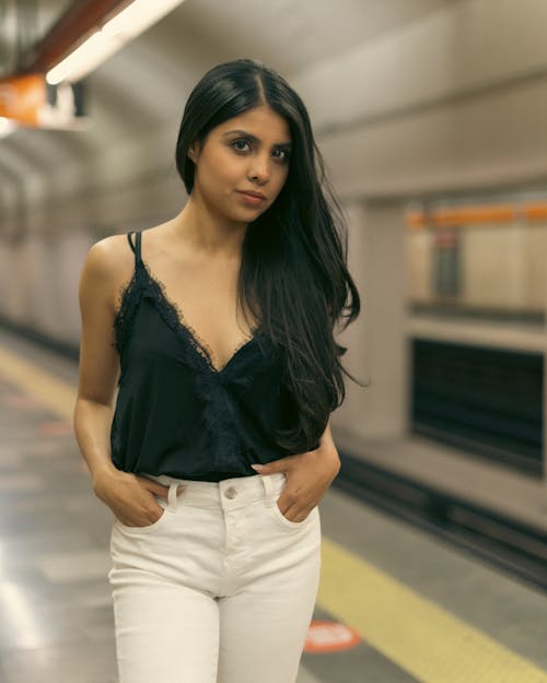A woman in black top and white pants standing in a subway station