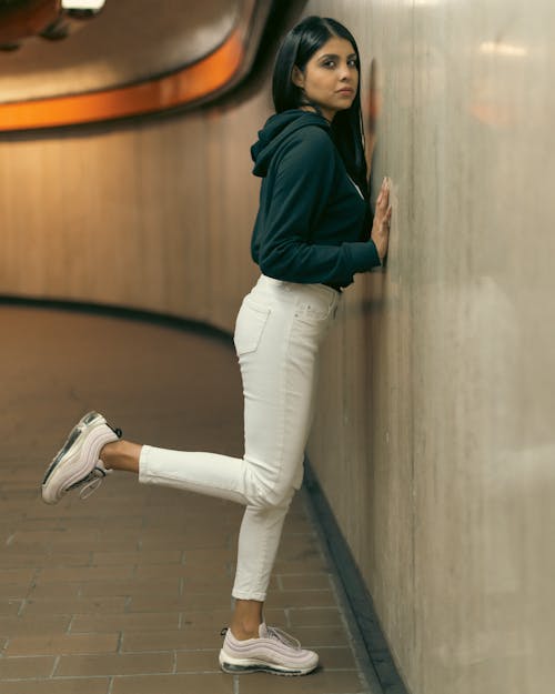A woman leaning against a wall in white pants