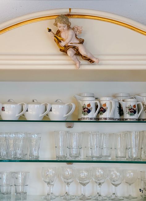 A refined display of glassware and porcelain cups on glass shelves adorned with a decorative cherub.