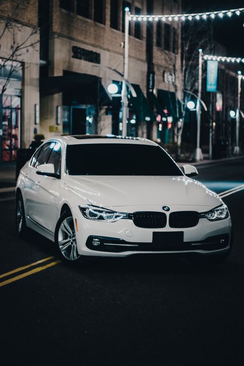 Free A sleek BMW 3 Series parked on a city street at night, showcasing modern elegance. Stock Photo