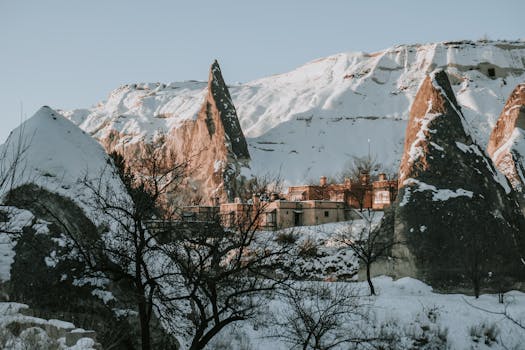 Snow-covered rock formations and a village in Cappadocia create a serene winter landscape.