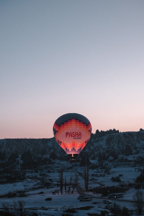 Free A hot air balloon floats over a snow-covered landscape at dusk, showcasing Cappadocia's unique scenery. Stock Photo
