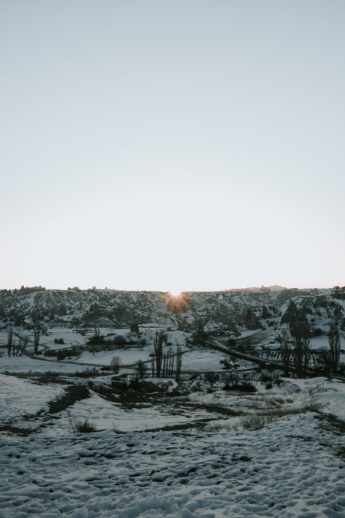 Free A tranquil winter landscape with snowy fields and a sunset peeking over the horizon. Stock Photo