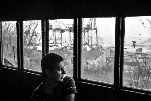 Free A man pensively gazes out a window overlooking the Valparaíso port, capturing solitude. Stock Photo
