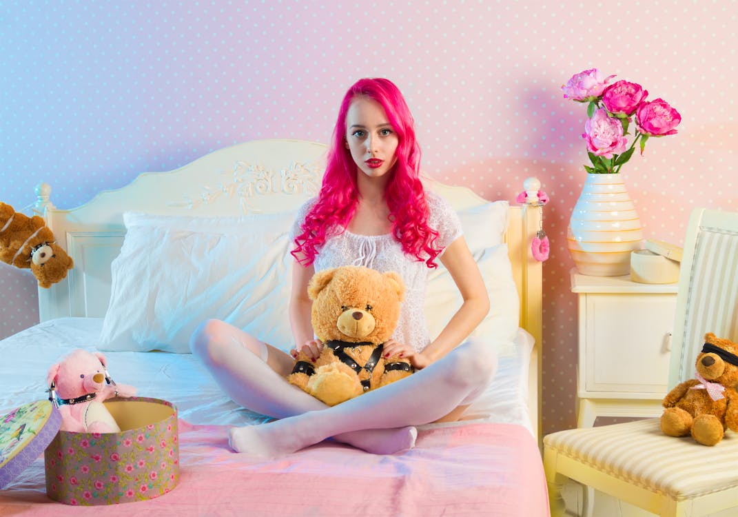 무료 일광에 곰 Plsuh 장난감 더블 침대에 앉아 분홍색 긴 머리 여자 스톡 사진
