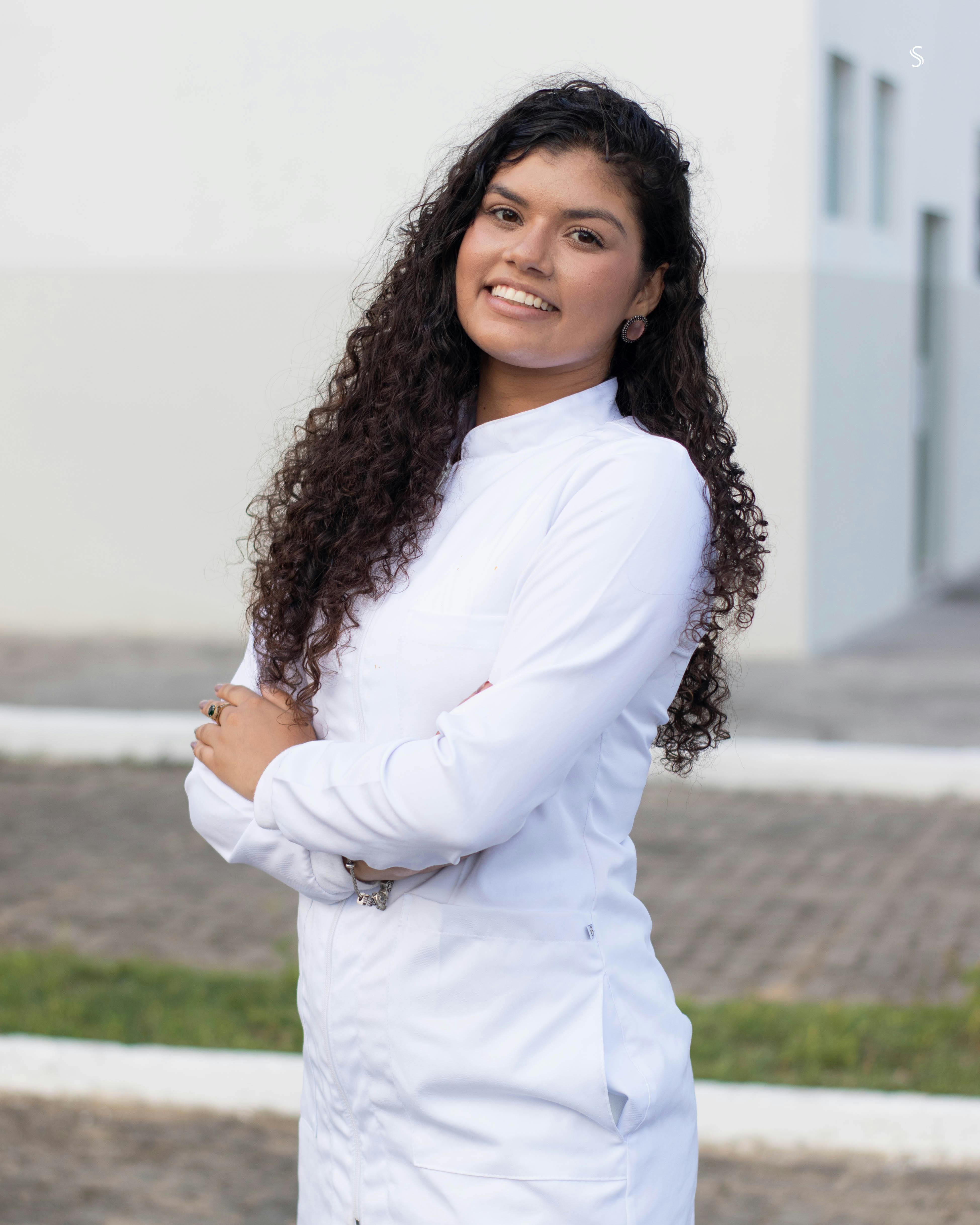 Confident woman with curly hair smiling in white attire, outdoors.