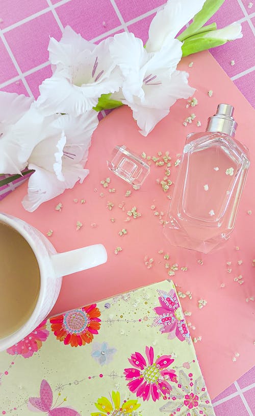 Top View of a Cup of Coffee and a Bottle of Perfume on a Pink Background with Flowers 