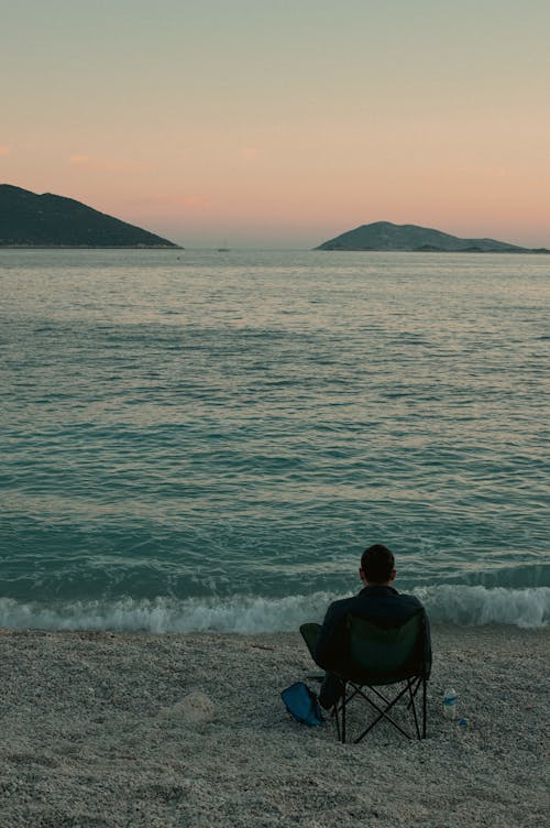 Back View of Man Sitting on a Beach at Sunset and Looking at the Sea 