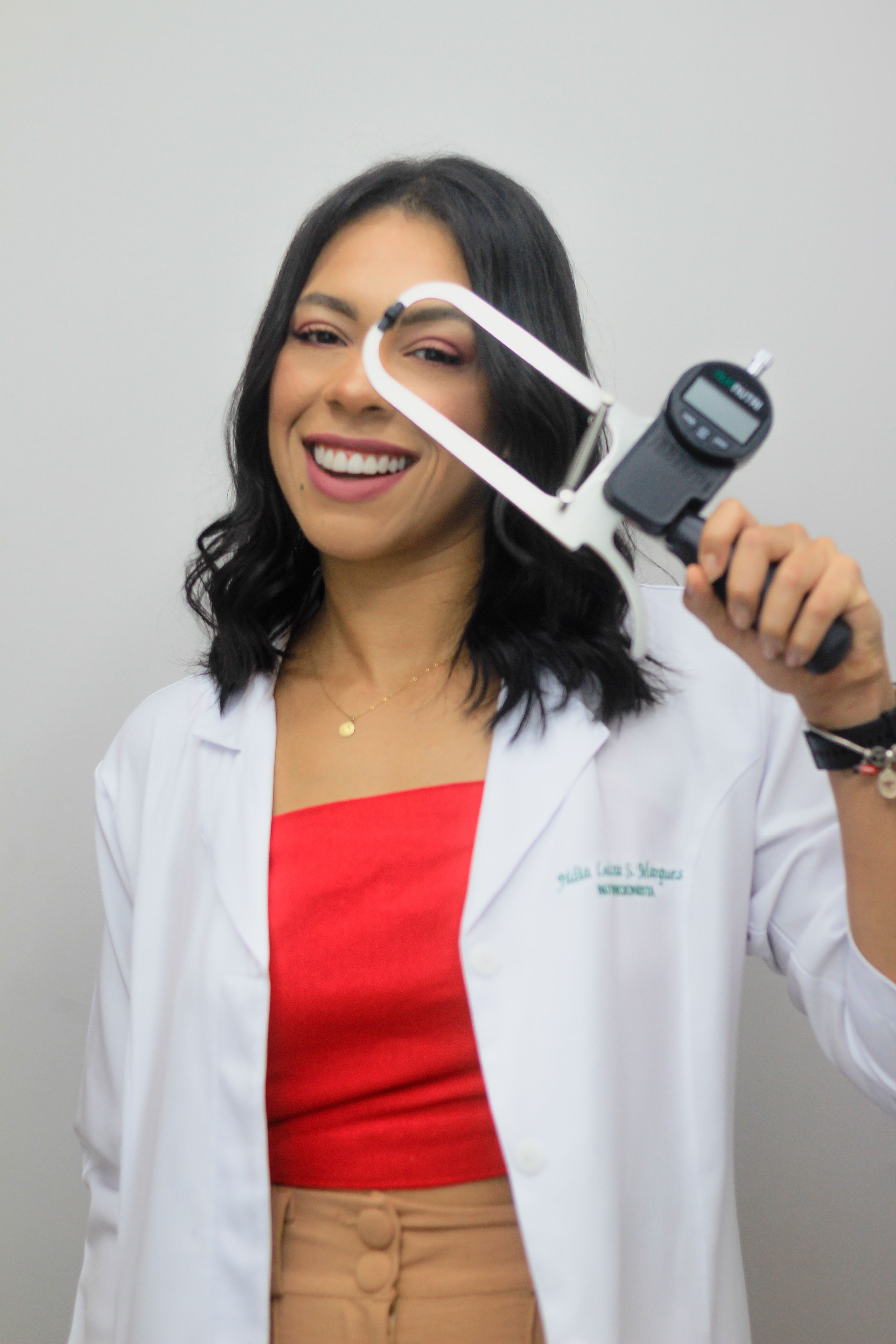 Smiling female doctor in lab coat holding a medical caliper on a gray background.