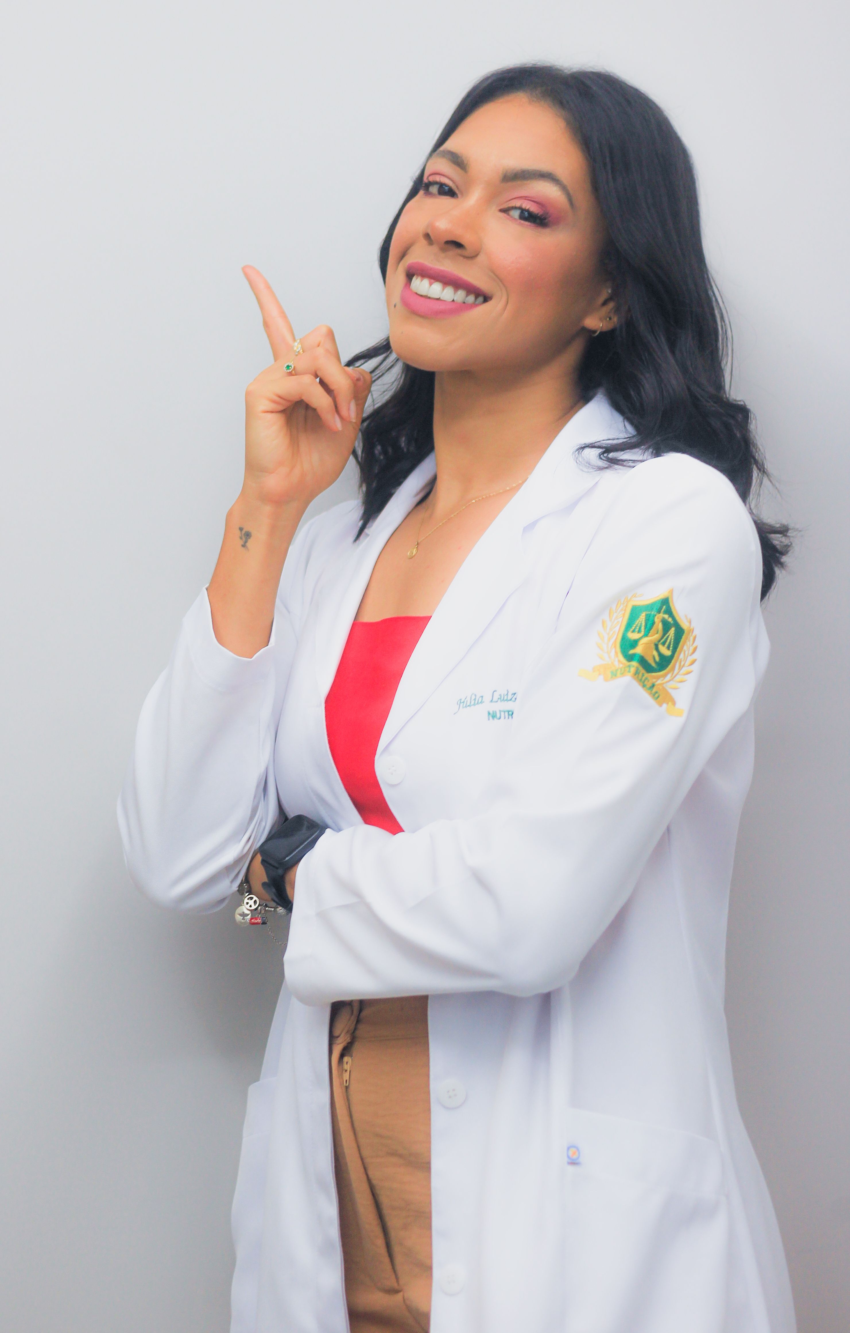 Portrait of a cheerful female doctor in a white coat, smiling confidently and pointing upwards.