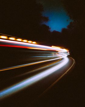 Captivating long-exposure shot of light trails on a forest road at night with a vivid blue sky.