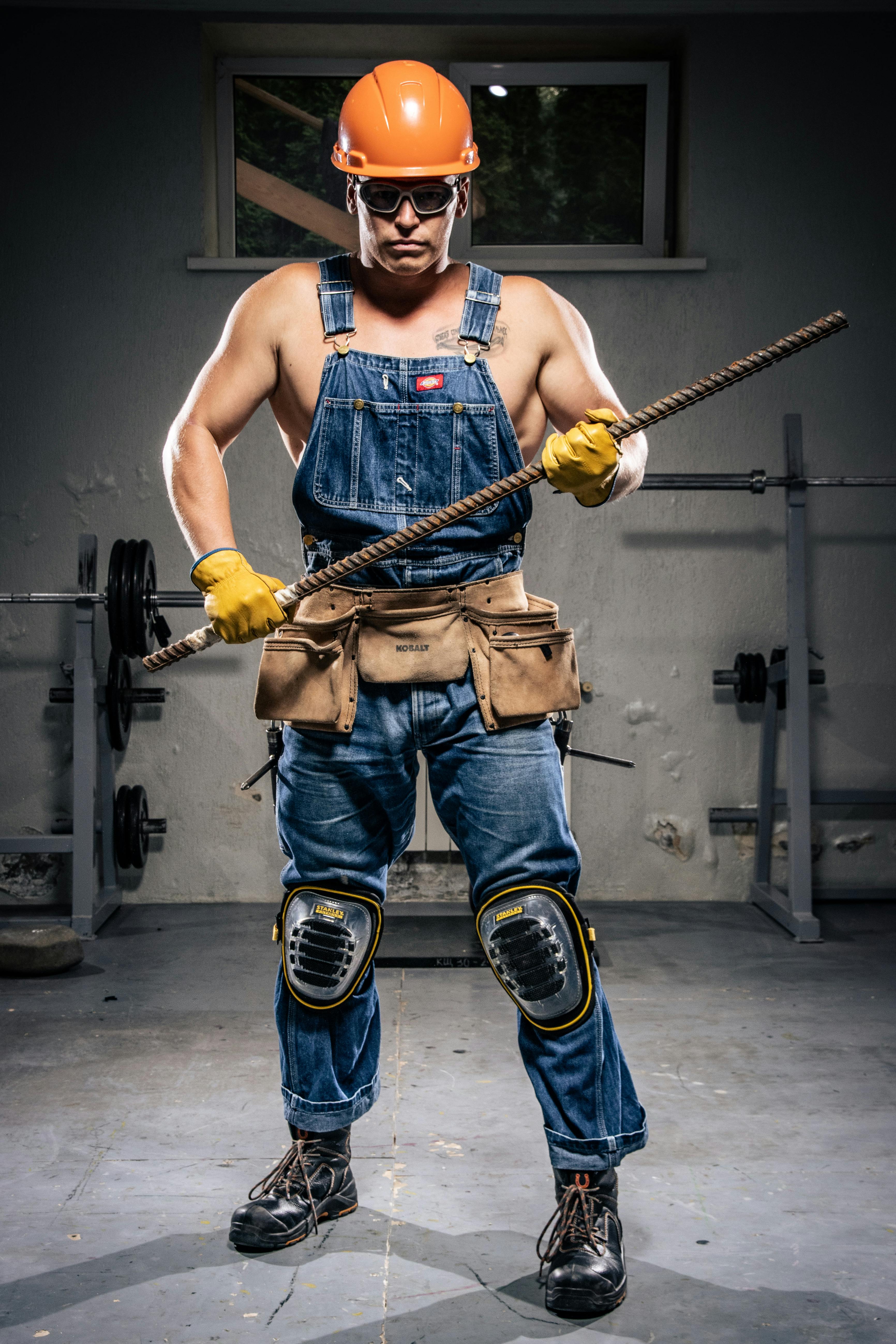 Portrait of a muscular construction worker wearing protective gear and holding rebar indoors.