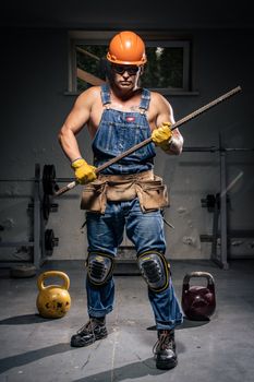 A strong construction worker in safety gear holding rebar in a gym setting.