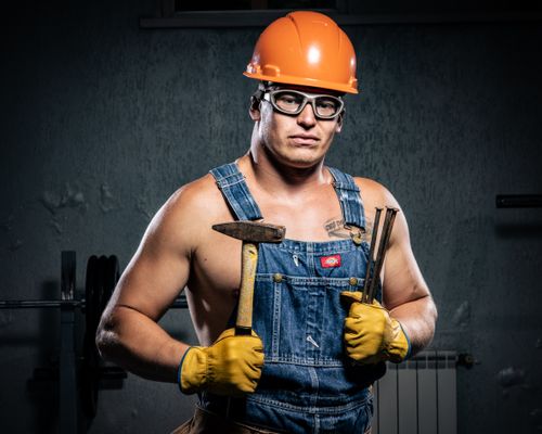 Free Portrait of a muscular construction worker wearing protective gear and holding tools indoors. Stock Photo