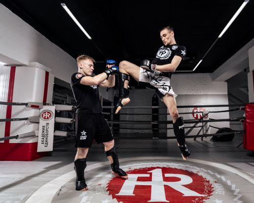 Free Two men practicing martial arts in a boxing ring, showcasing a dynamic jumping kick. Stock Photo