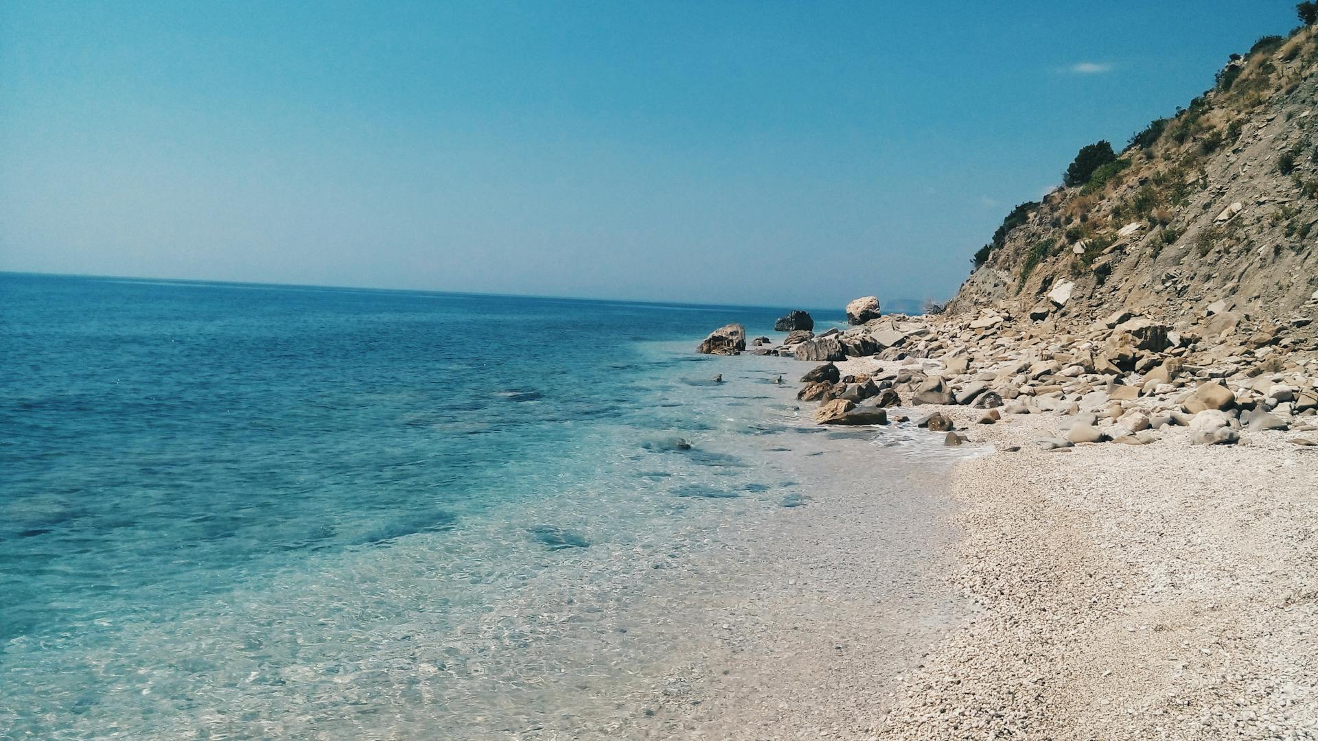 Beautiful clear blue ocean meeting a rocky coastline under a sunny sky.