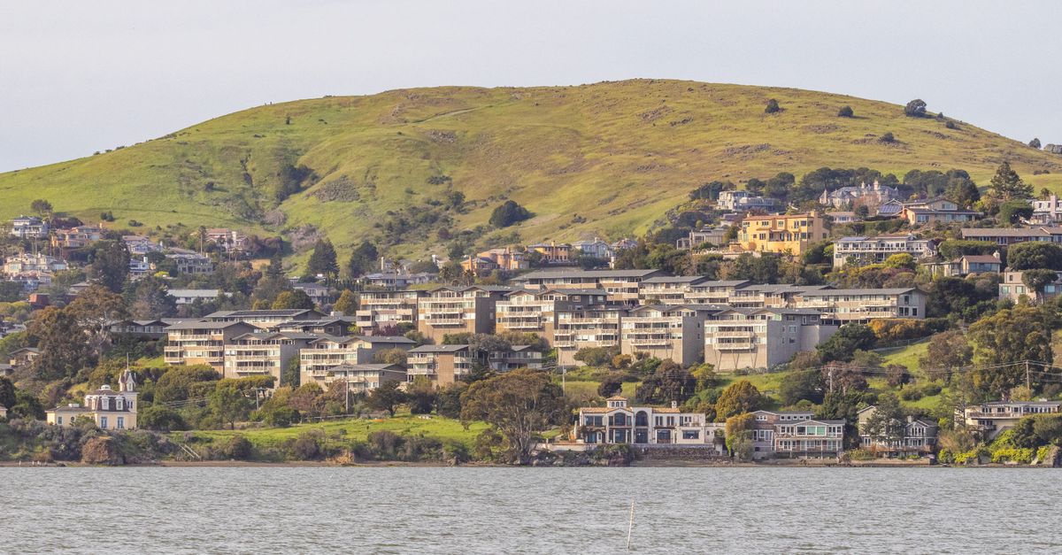 Picturesque hillside town with waterfront view, featuring lush green hills and residential buildings.
