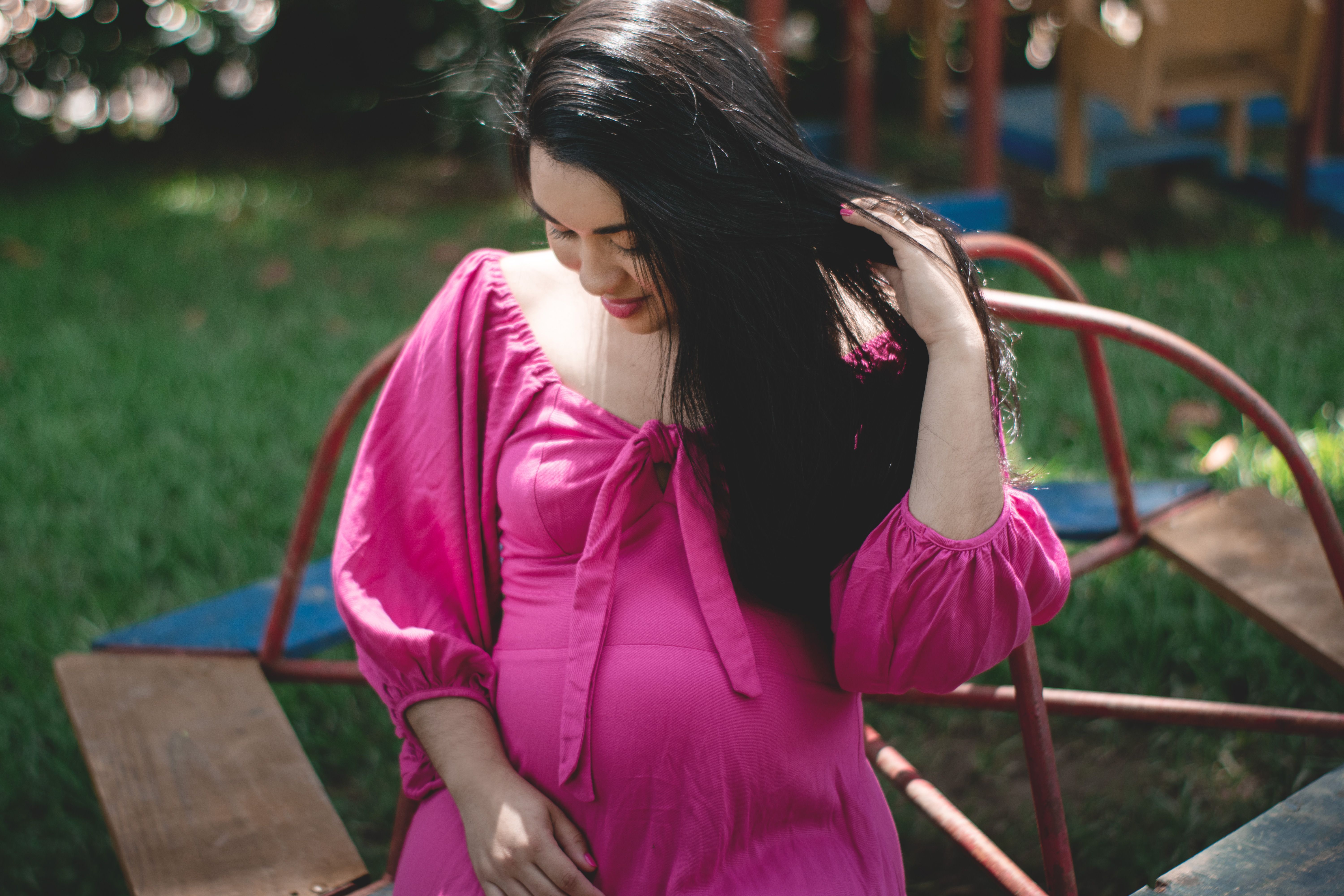 A serene portrait of a pregnant woman in a pink dress enjoying a calm moment outdoors.