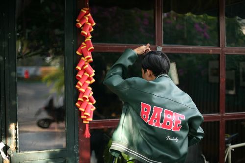 Free Stylish person with 'BABE' jacket standing outdoors, green and red tones. Stock Photo