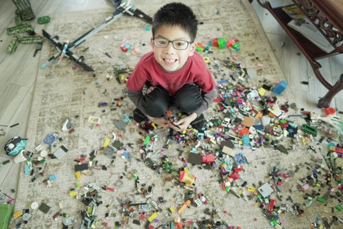 Free Young boy smiling while surrounded by colorful building blocks on a carpet indoors. Stock Photo