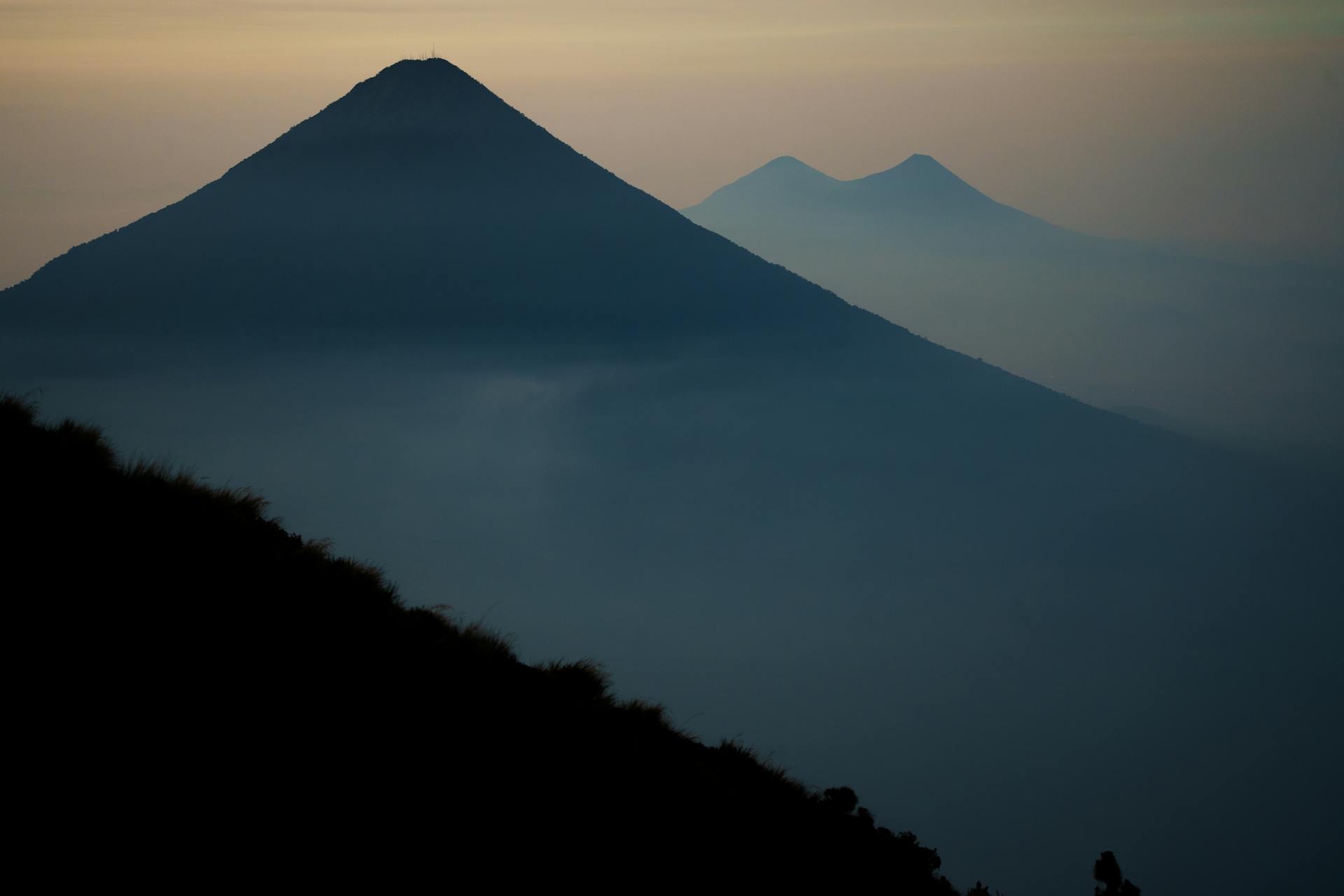 Scenic view of silhouetted volcanic mountains in Guatemala at sunrise, surrounded by mist.