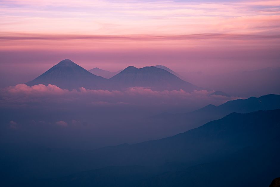 A breathtaking view of mountains under a pastel twilight sky, surrounded by clouds.