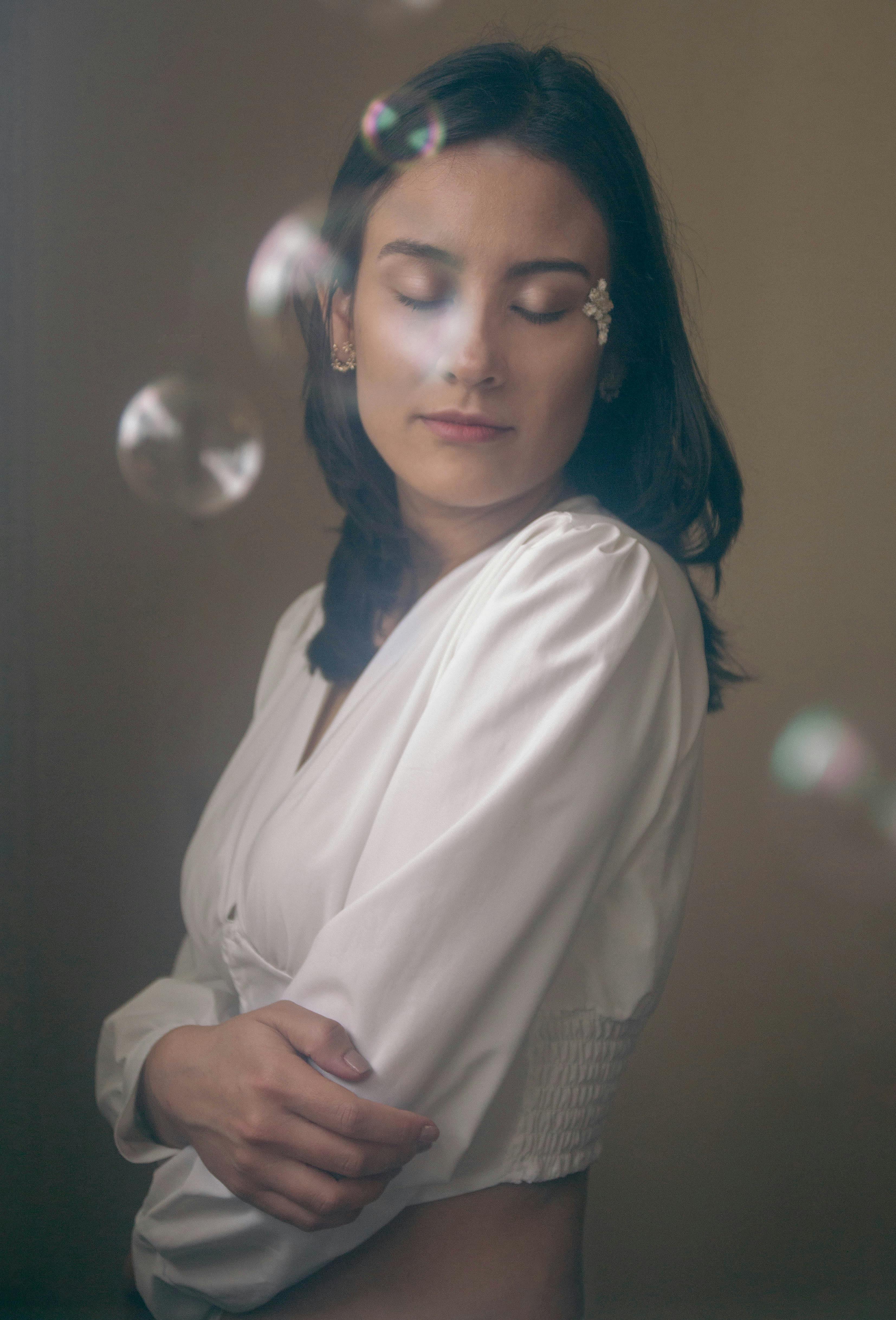Elegant portrait of a young brunette woman with closed eyes and soap bubbles floating around her.