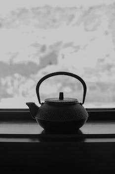 Elegant black teapot silhouette against a blurred window background, exuding a minimalistic and artistic vibe.