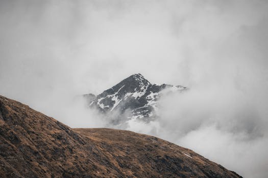 A captivating view of a snow-capped mountain peak shrouded in mist and clouds, evoking mystery and tranquility.