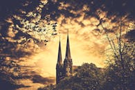 哥特式教堂的尖顶在树木环绕的日落天空中耸立