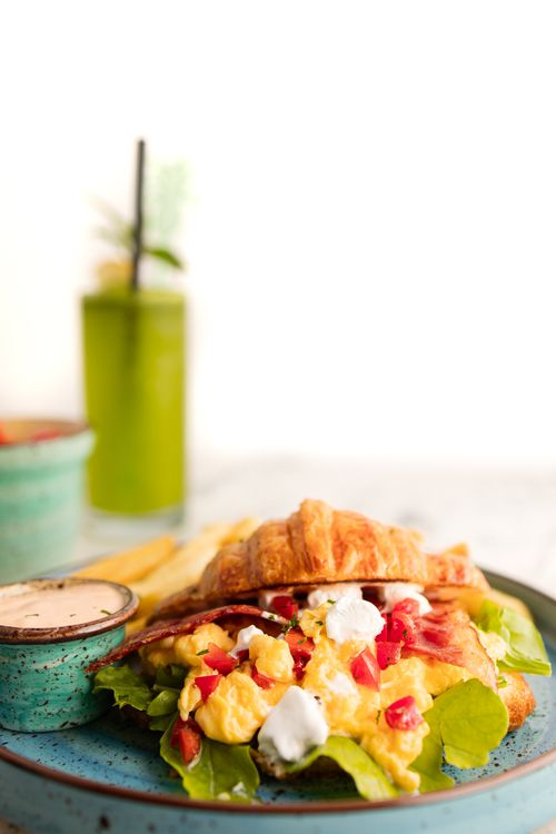 Free Scrumptious breakfast croissant with bacon, scrambled eggs, and greens on a blue plate. Stock Photo