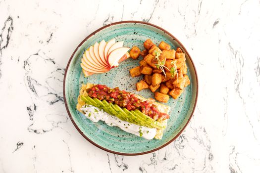 Delicious avocado toast with apples and crispy potatoes on a turquoise plate.