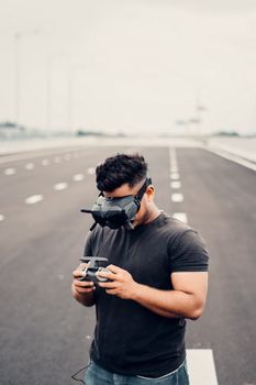 Young man using VR goggles and drone controller on empty road