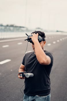 A man wearing VR goggles and controlling a drone on an empty street.