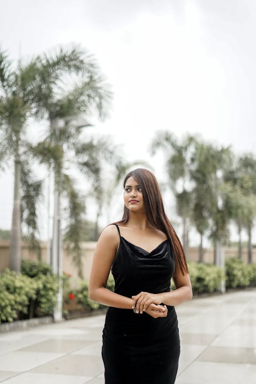 Young Woman in a Black Dress Standing on the Background of Palm Trees 