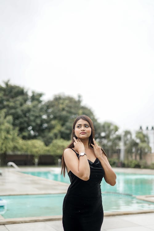 Young Woman in a Black Dress Standing by the Swimming Pool 