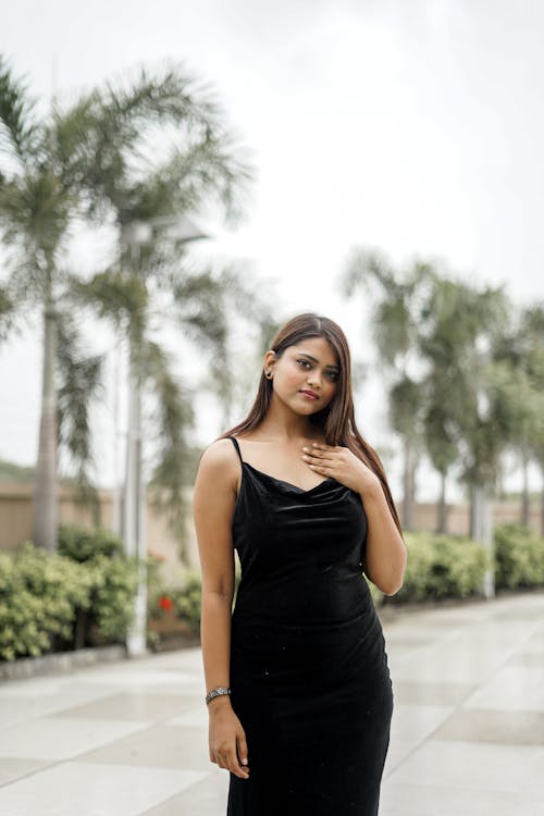 Young Woman in a Black Dress Standing on the Background of Palm Trees 