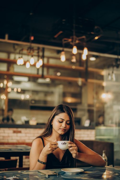 Free Woman savoring a warm cup of coffee in a stylish café with ambient lighting. Stock Photo