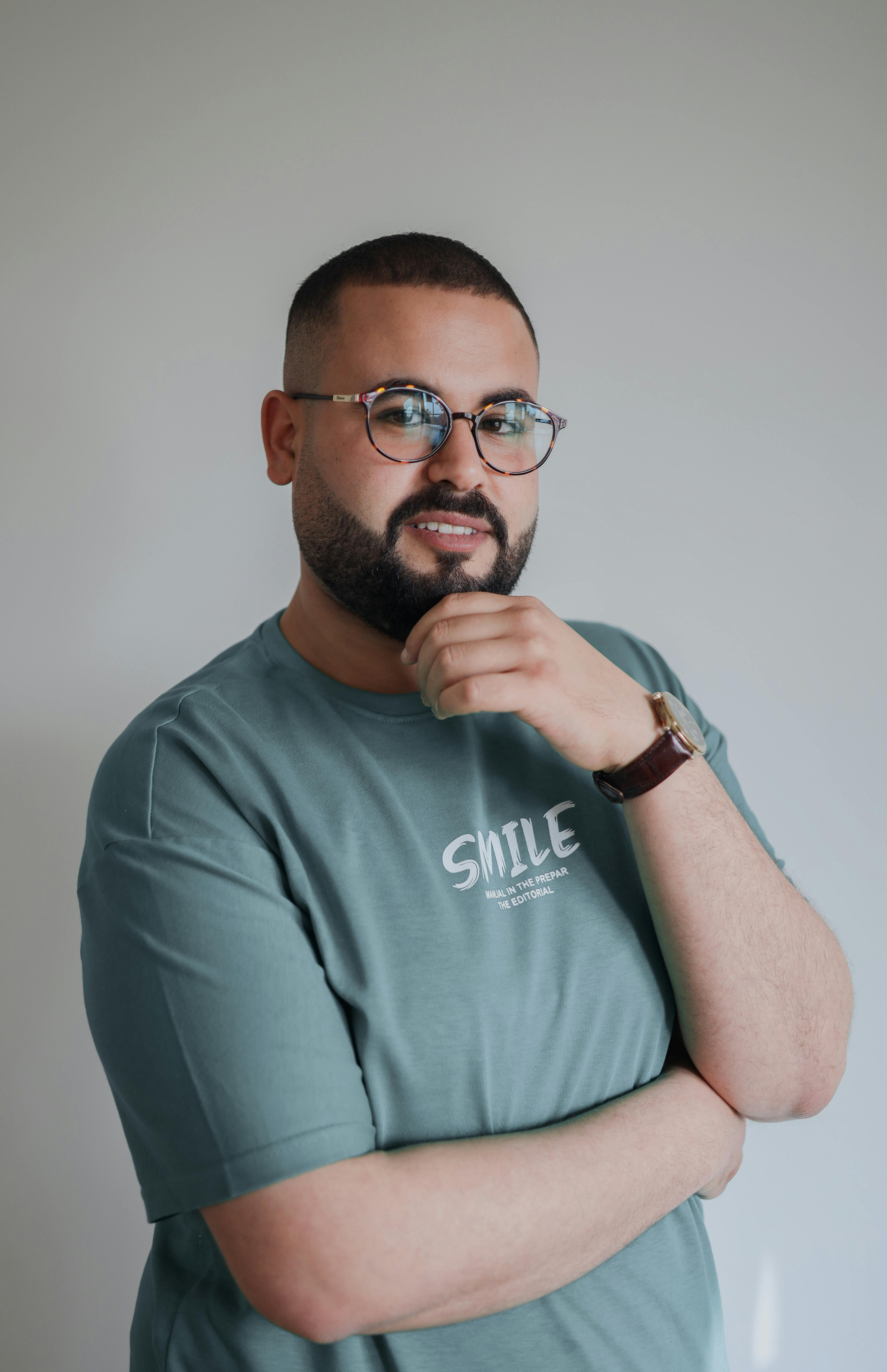 Portrait of a confident man with glasses and beard, wearing a smile t-shirt, in a studio setting.